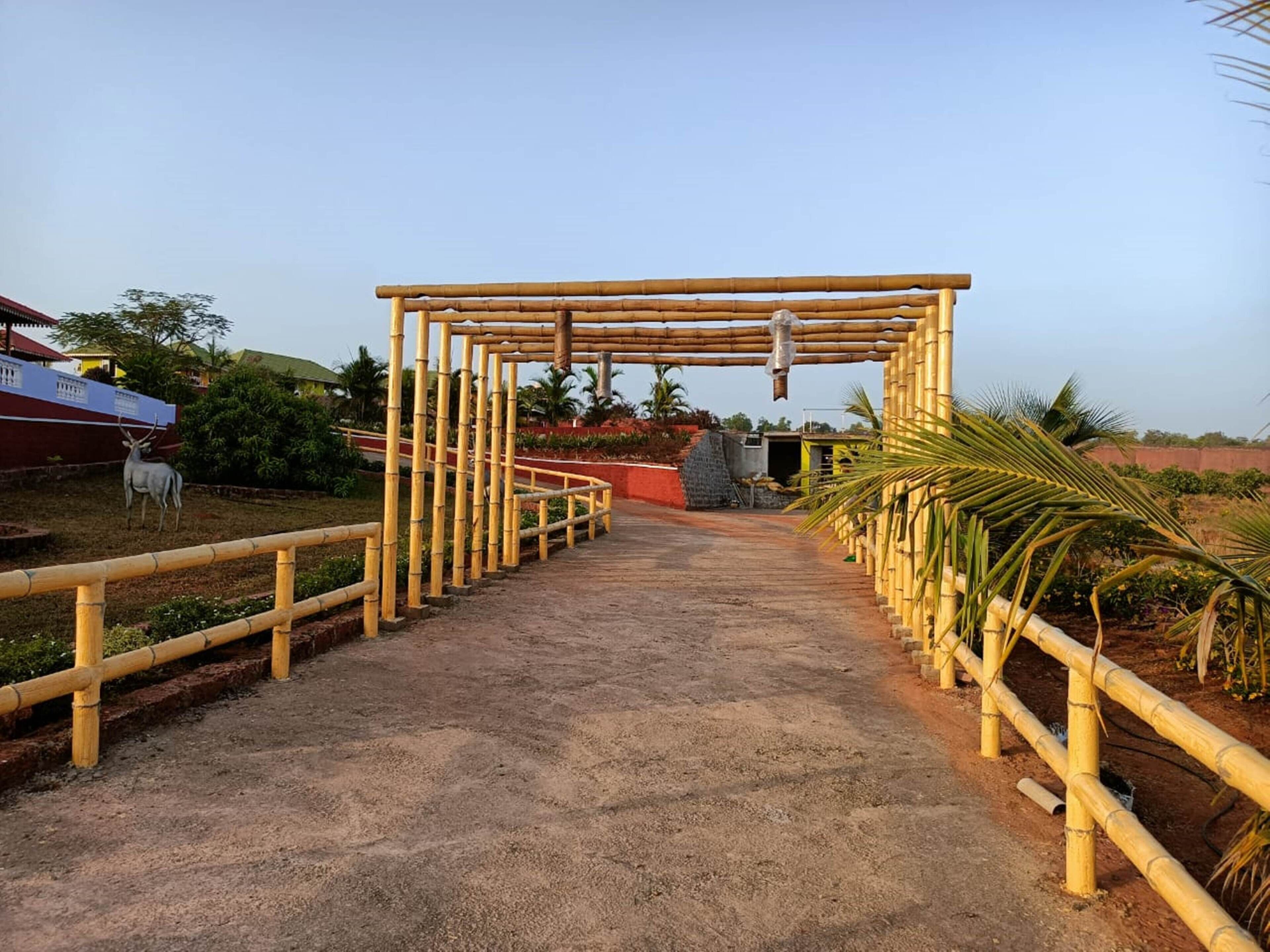 A bamboo archway leading to a sandy path with a statue of a deer on the left.