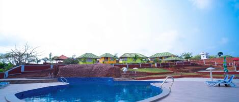 A swimming pool with a tiled deck, a few lounge chairs, and a building with a red roof in the background.