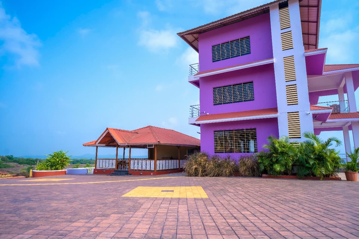A multi-story building with a purple facade, a red-roofed structure in the foreground, and a paved area with potted plants.