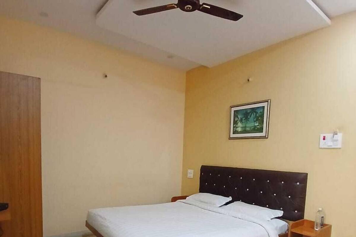 A bedroom with a bed, a chair, a bedside table, a nightstand, a ceiling fan, and a framed picture on the wall.