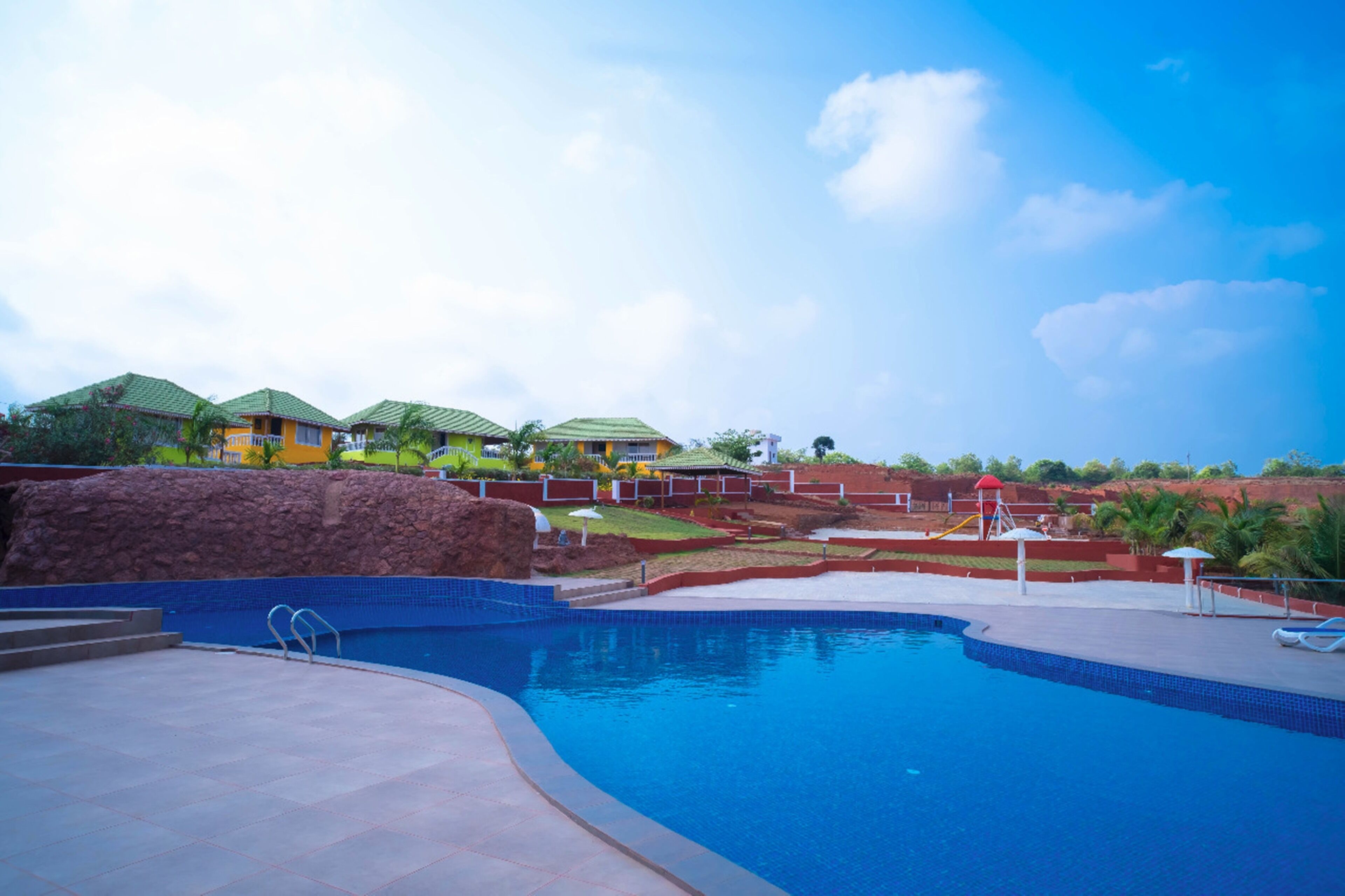 A swimming pool with a stone wall, a water slide, and a red water tower.