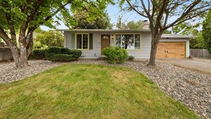 Ein eingeschossiges Haus mit Veranda, Garage und gepflegtem Rasen.