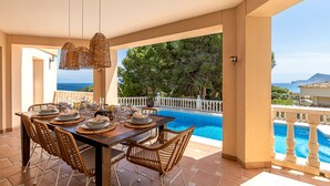 An outdoor dining area with a pool view, wicker chairs, and a table set for dining. - Belle Vue - Altea, Costa Blanca (Altea)