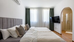A hotel room with a large bed, a flat-screen TV, a shower area, and a window with curtains. - Belle Vue - Altea, Costa Blanca (Altea)