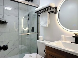 A modern bathroom with a glass-enclosed shower, a white sink, and a vanity with a mirror. - Departure Bay Motel (Nanaimo)