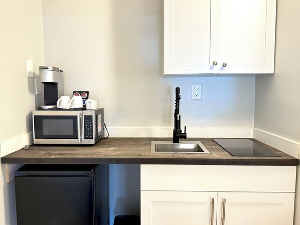 Una cocina compacta equipada con microondas, cafetera y pileta.