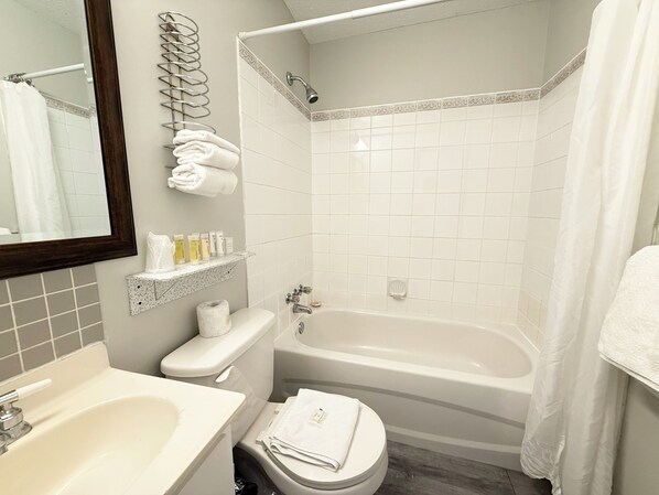 A bathroom with a sink, toilet, and bathtub. There are towels and toiletries on the wall. - Departure Bay Motel (Nanaimo)