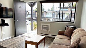 Ein modernes Wohnzimmer mit einer Couch, einem Couchtisch, einem an der Wand befestigten Fernseher und einem großen Fenster mit Blick nach draußen.