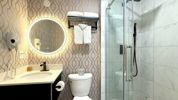 A modern bathroom with a patterned wall, a round mirror, a toilet, a glass shower enclosure, and a towel rack.