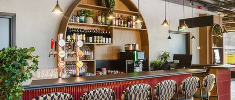 Una zona de bar con mostrador, taburetes y estantes llenos de botellas y copas.