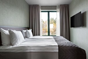 A hotel room with a large bed, a flat-screen TV mounted on the wall, and a window with curtains.