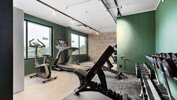 A gym with cardio machines, weightlifting equipment, and a large window offering a city view.