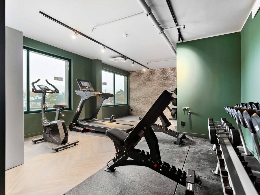 A gym with cardio machines, weightlifting equipment, and a large window offering a city view.