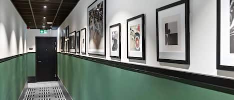 Un couloir avec des œuvres d’art encadrées accrochées aux murs, un sol à motifs et une décoration murale aux tons verts et blancs.