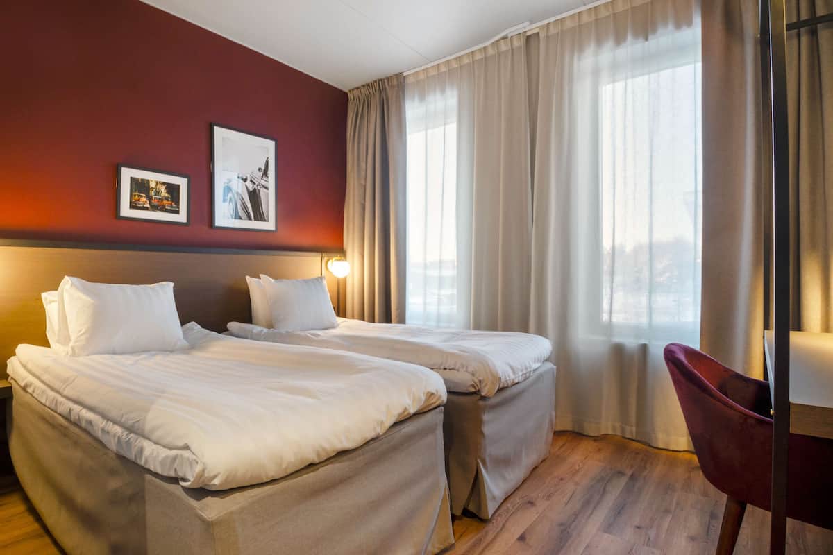 A hotel room with two beds, a desk, a chair, and a large window with curtains.