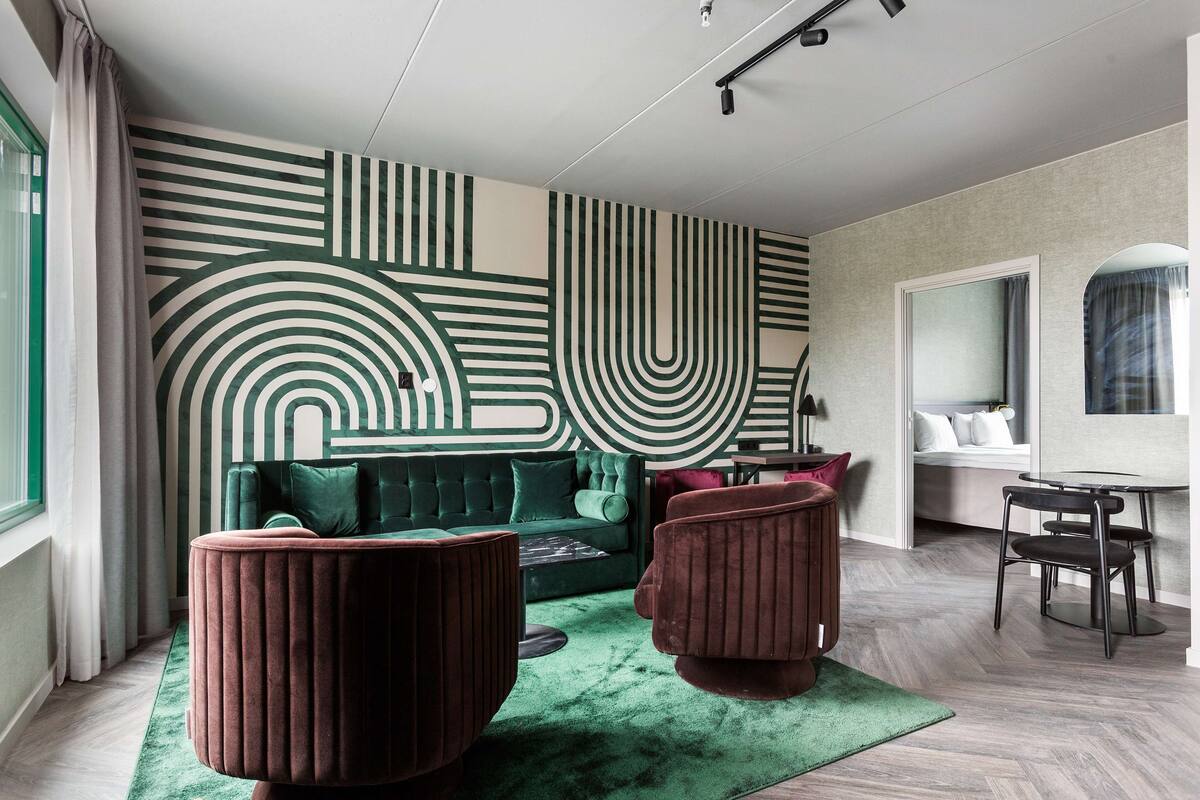 A modern living room with a green sofa, two red ottomans, a coffee table, and a patterned wall.