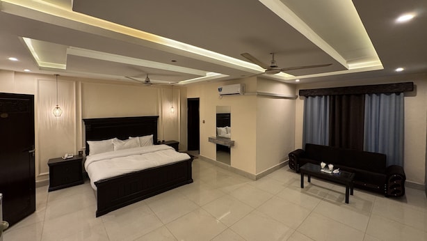 A modern hotel room with a large bed, a sofa, a small table, a ceiling fan, and recessed lighting.