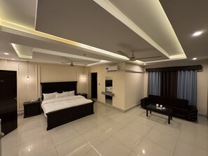 Una habitación de hotel moderna con una cama grande, un sofá, una mesita pequeña, un ventilador de techo e iluminación empotrada.