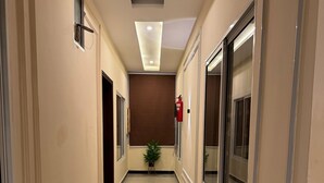A clean, well-lit hallway with a fire extinguisher mounted on the wall, a potted plant, and a door at the end.