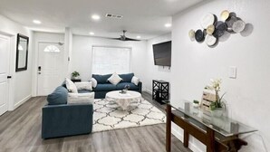 Un salon moderne avec un canapé bleu, une table basse et un coin repas comprenant une table et des chaises en verre.
