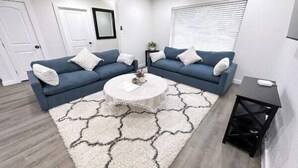 Un salon moderne avec deux canapés bleus, une table basse ronde et un tapis blanc orné d’un motif géométrique.