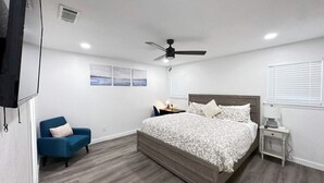 Une chambre à coucher avec un lit, un ventilateur de plafond, une table de chevet, une chaise et une fenêtre.