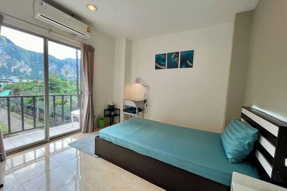 Ein Hotelzimmer mit Bett, Schreibtisch, Stuhl, Lampe und Blick auf Berge durch ein großes Fenster.