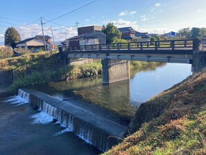 A bridge over a calm waterway with a small waterfall, surrounded by residential buildings and greenery.