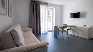 A modern living room with a sofa, a dining table with chairs, a TV mounted on the wall, and a sliding glass door leading to a balcony. - Nautika Suites  (Alghero)