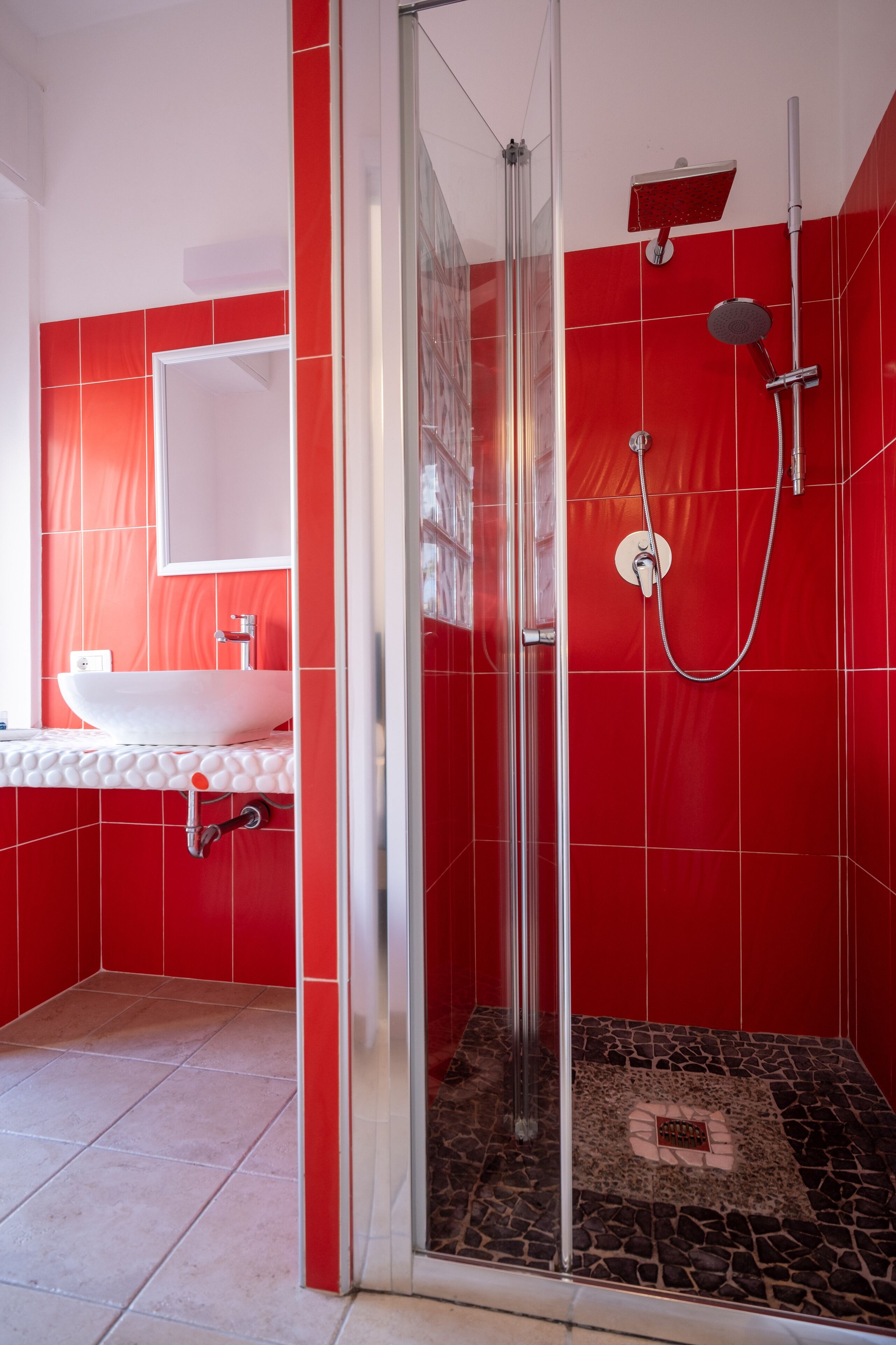 A modern bathroom with a glass-enclosed shower, a white sink, and red tiled walls.