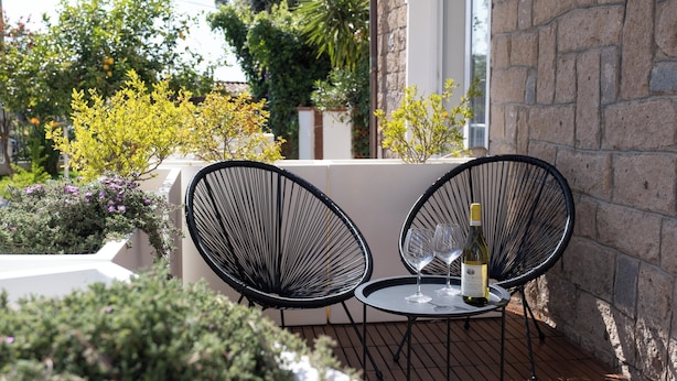 A patio with two black wire chairs and a small round table, a bottle of wine, and a glass on the table. - Nautika Suites  (Alghero)