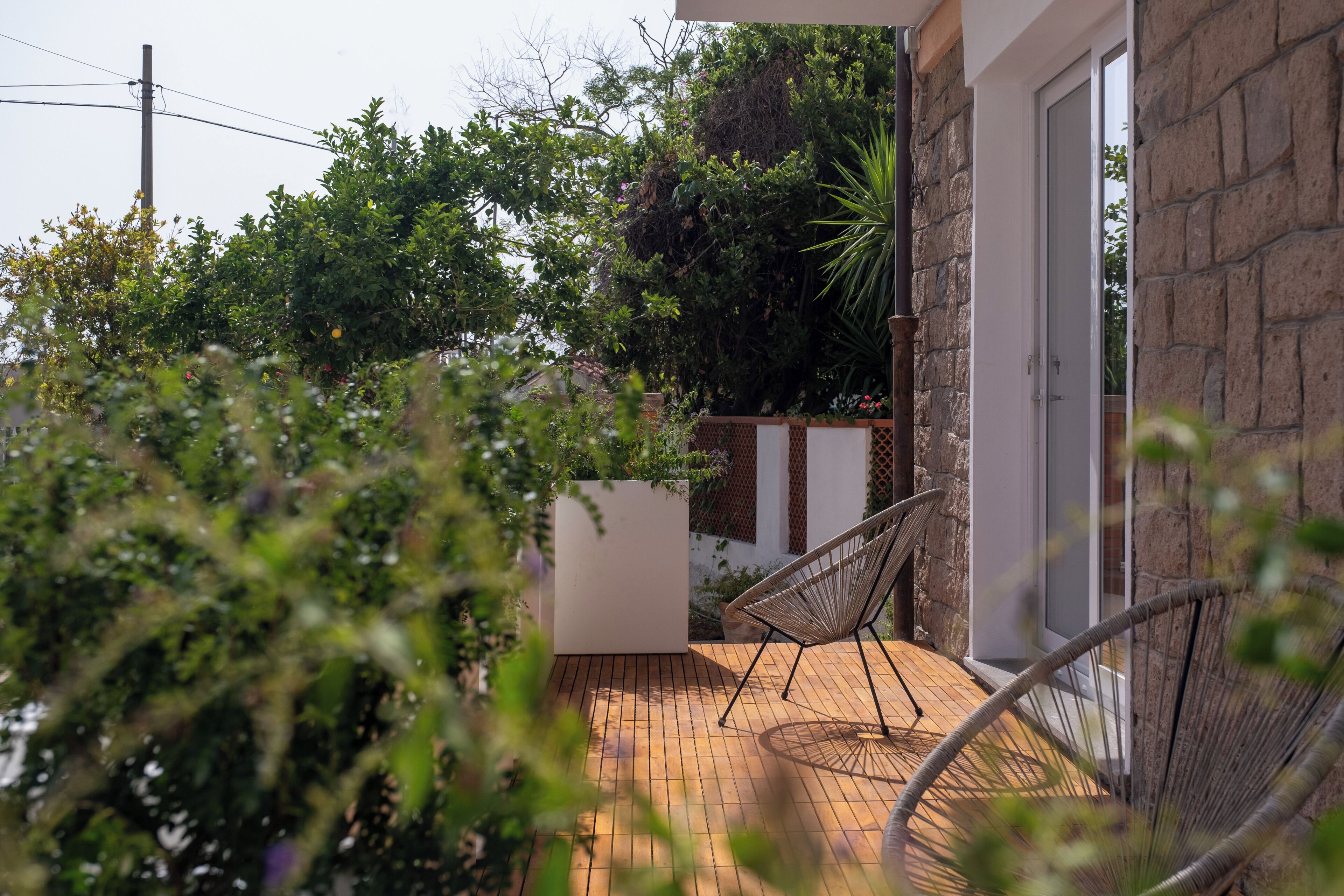 A patio with a wooden deck, a white planter, and a wicker chair.