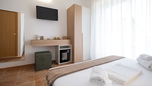 A modern hotel room with a bed, a flat-screen TV mounted on the wall, a wooden wardrobe, and a small seating area with a coffee machine. - Nautika Suites  (Alghero)