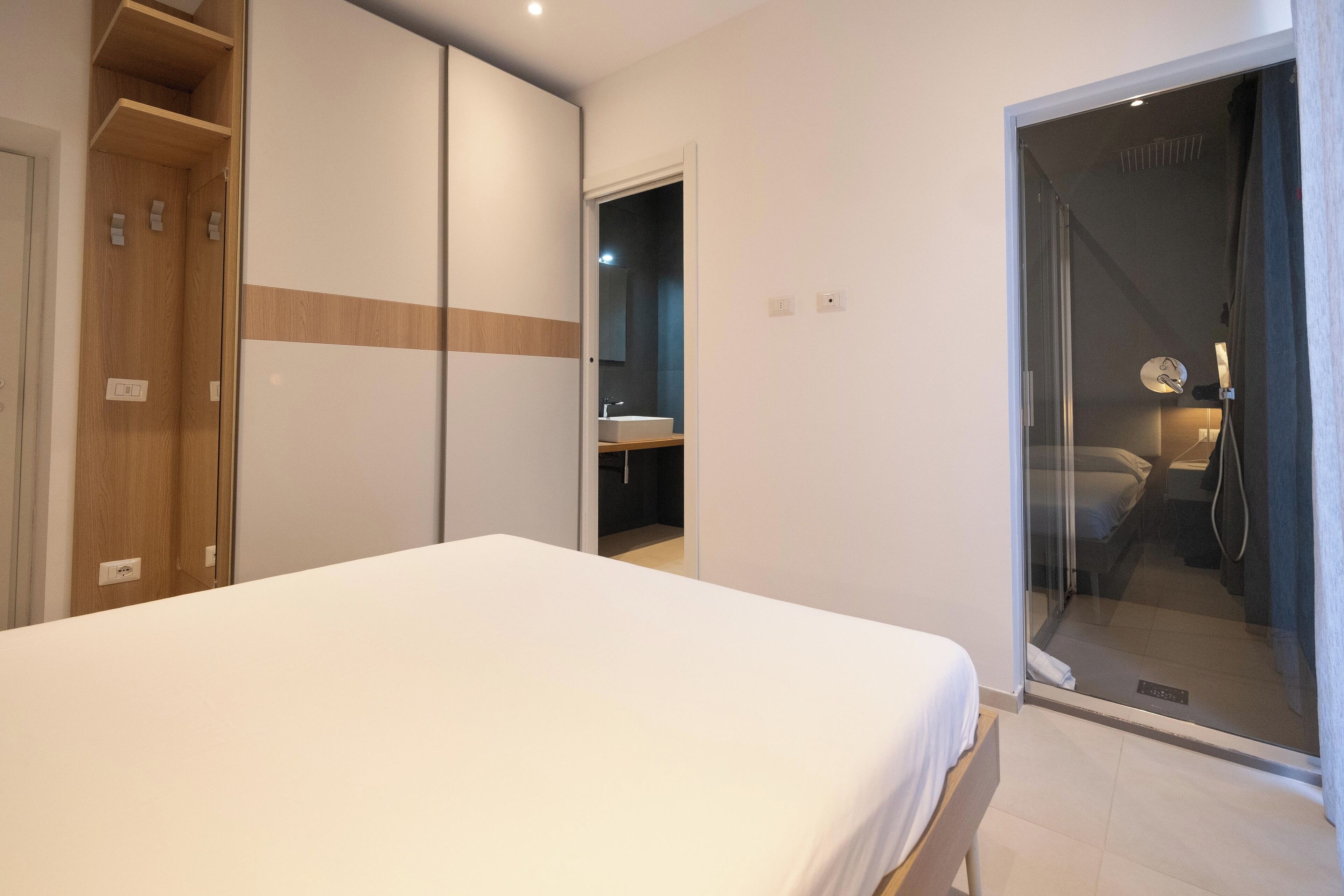 A bedroom with a bed, a wardrobe, a bathroom visible through a glass door, and a shower area.