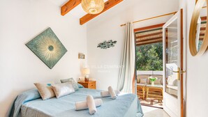 Une chambre à coucher comprenant un lit, des oreillers, une œuvre d’art murale, une table de chevet et une vue sur un espace extérieur aménagé pour s’asseoir.