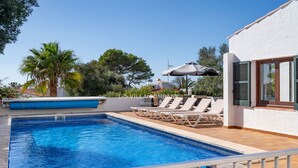 Une piscine entourée de verdure et d’un bâtiment blanc, avec des chaises longues et des parasols.