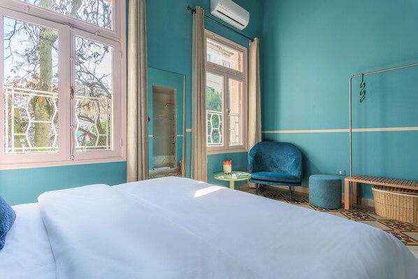 A room with a bed, a blue chair, a small round table, and a window with curtains.