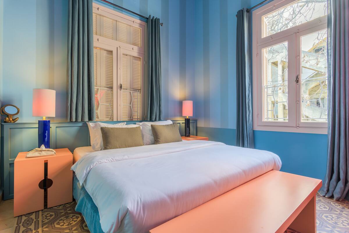 A bedroom with a bed, bedside tables, lamps, a window with curtains, and a view of the outside.