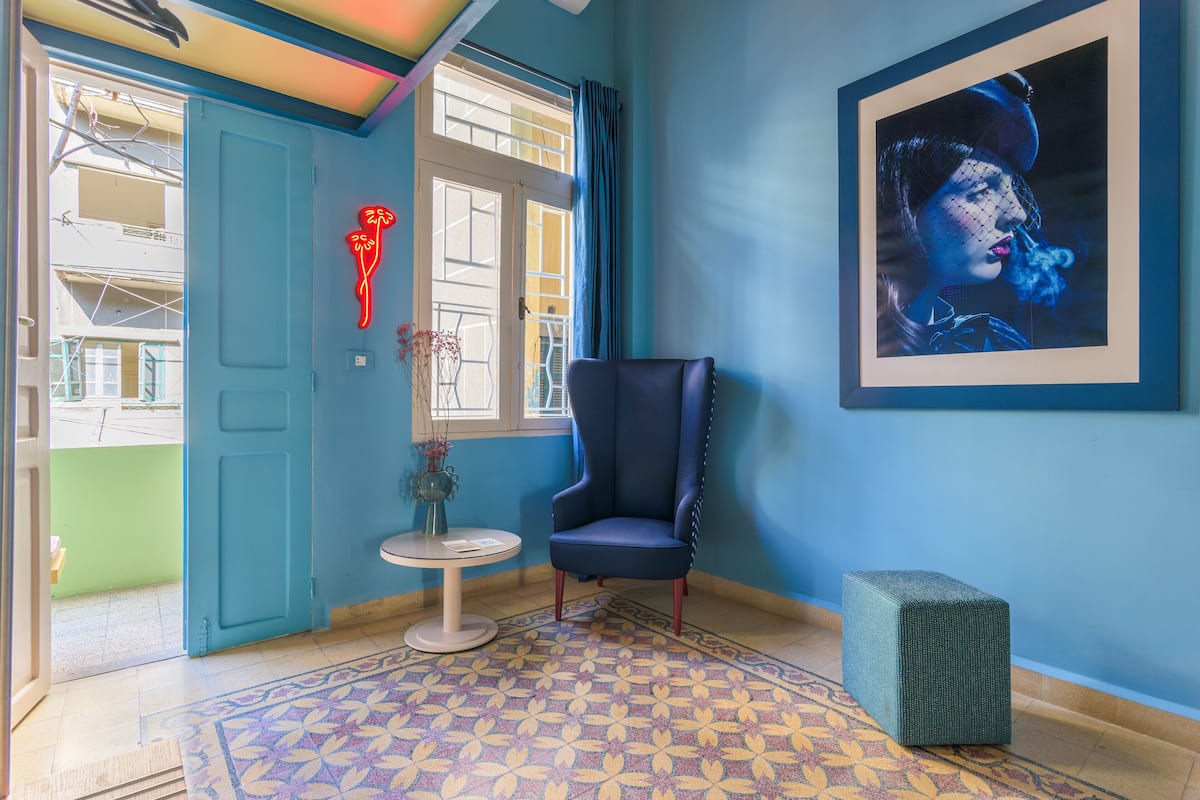 A room with a blue chair, a small table with a vase, a framed picture on the wall, and a patterned rug.