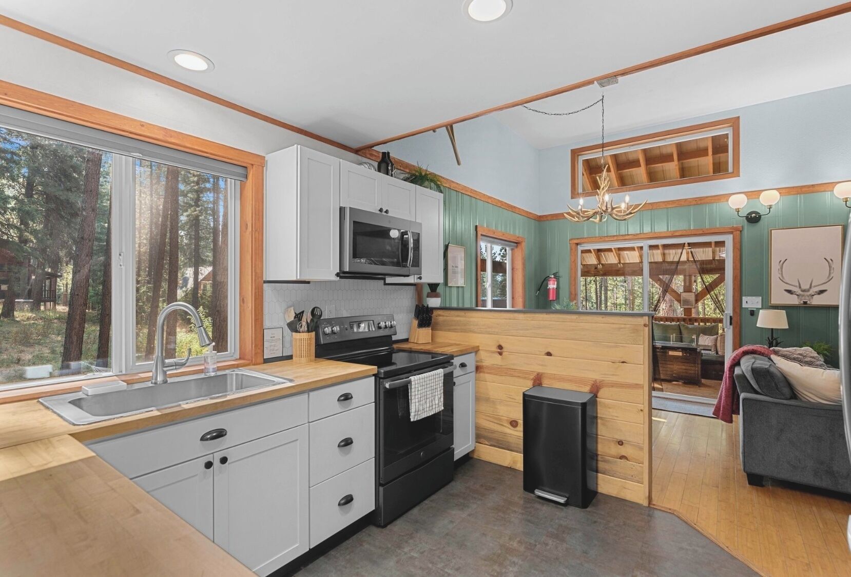 A modern kitchen with white cabinets, a black stove, and a microwave. There is a large window providing a view of the outdoors.