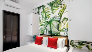 Quarto com uma cama grande, cabeceira com design trançado e parede com um mural de folhas tropicais.