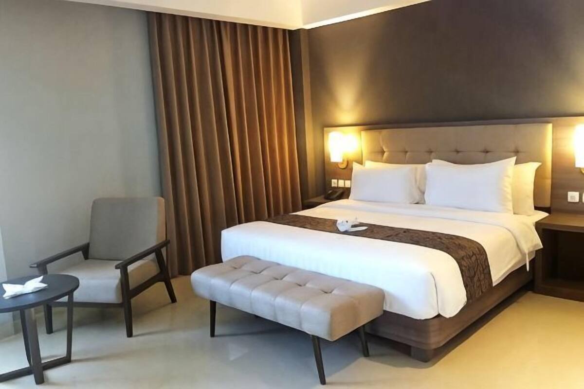 A hotel room with a bed, a chair, a small table, and a bench.