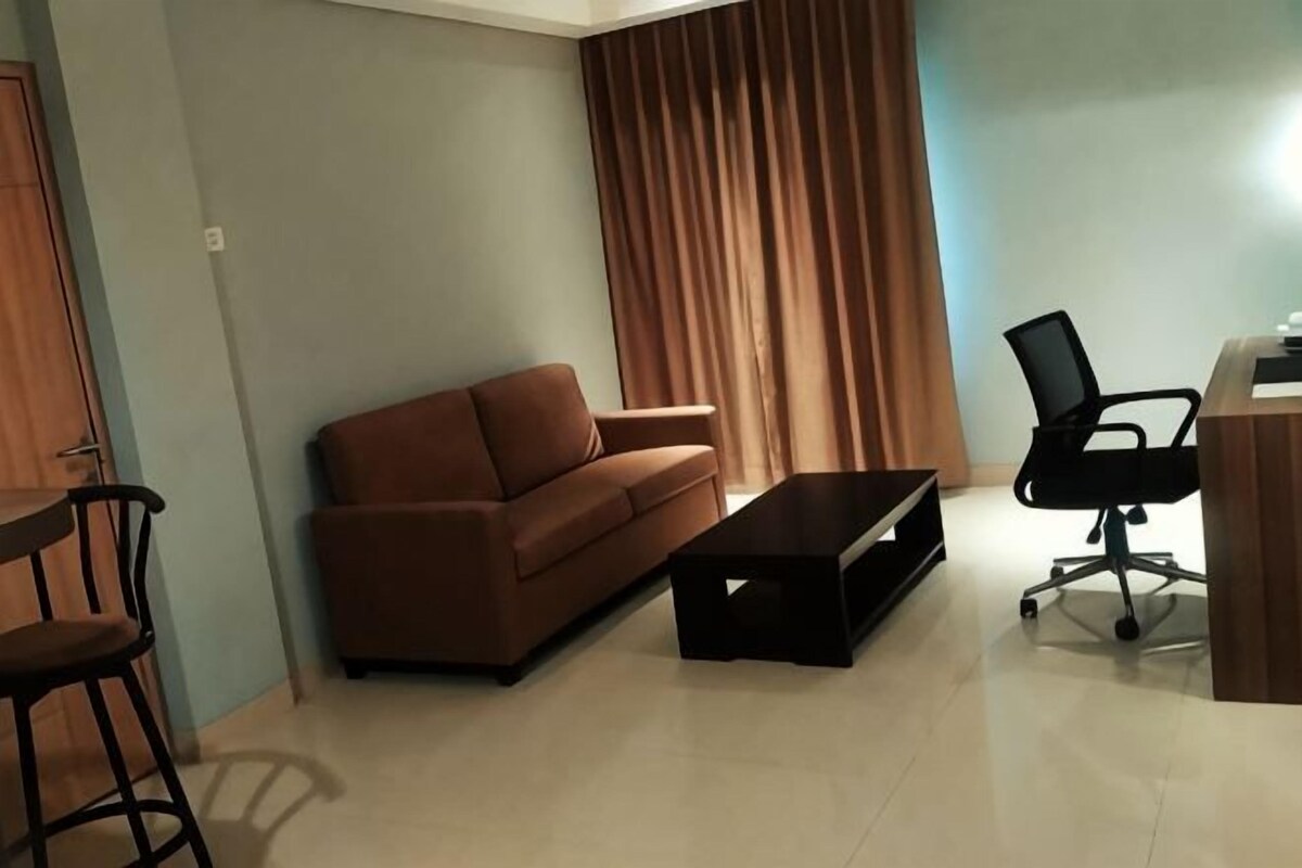 A living room with a sofa, a coffee table, a chair, and a desk with a chair.
