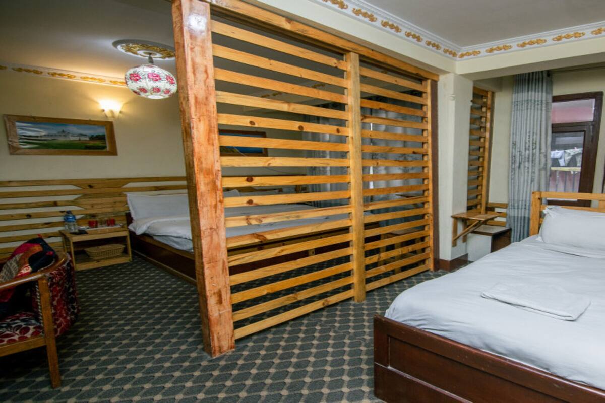 Une pièce comprenant un lit en bois, une armoire en bois, une chaise en bois, une petite table et une lampe fixée au mur.