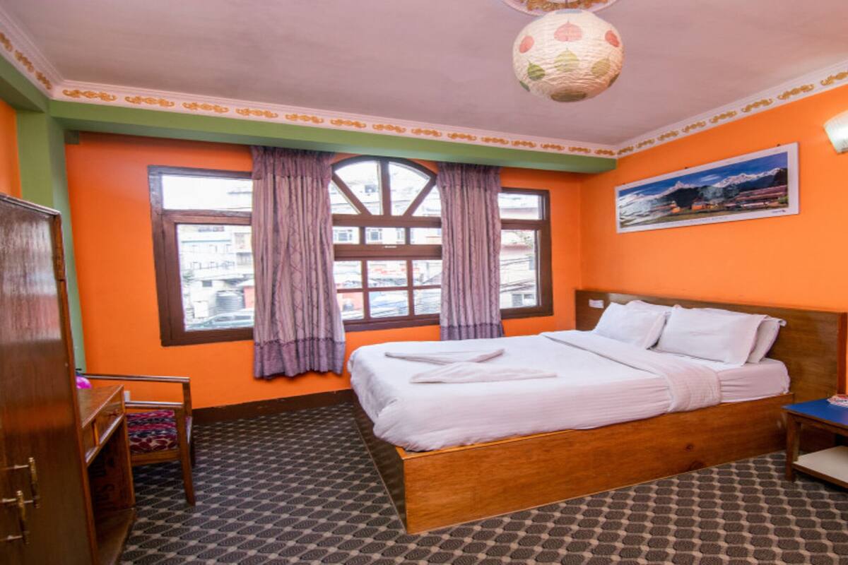 Une chambre d’hôtel avec un lit en bois, un bureau, une chaise, une armoire, une fenêtre avec des rideaux et un tableau au mur.