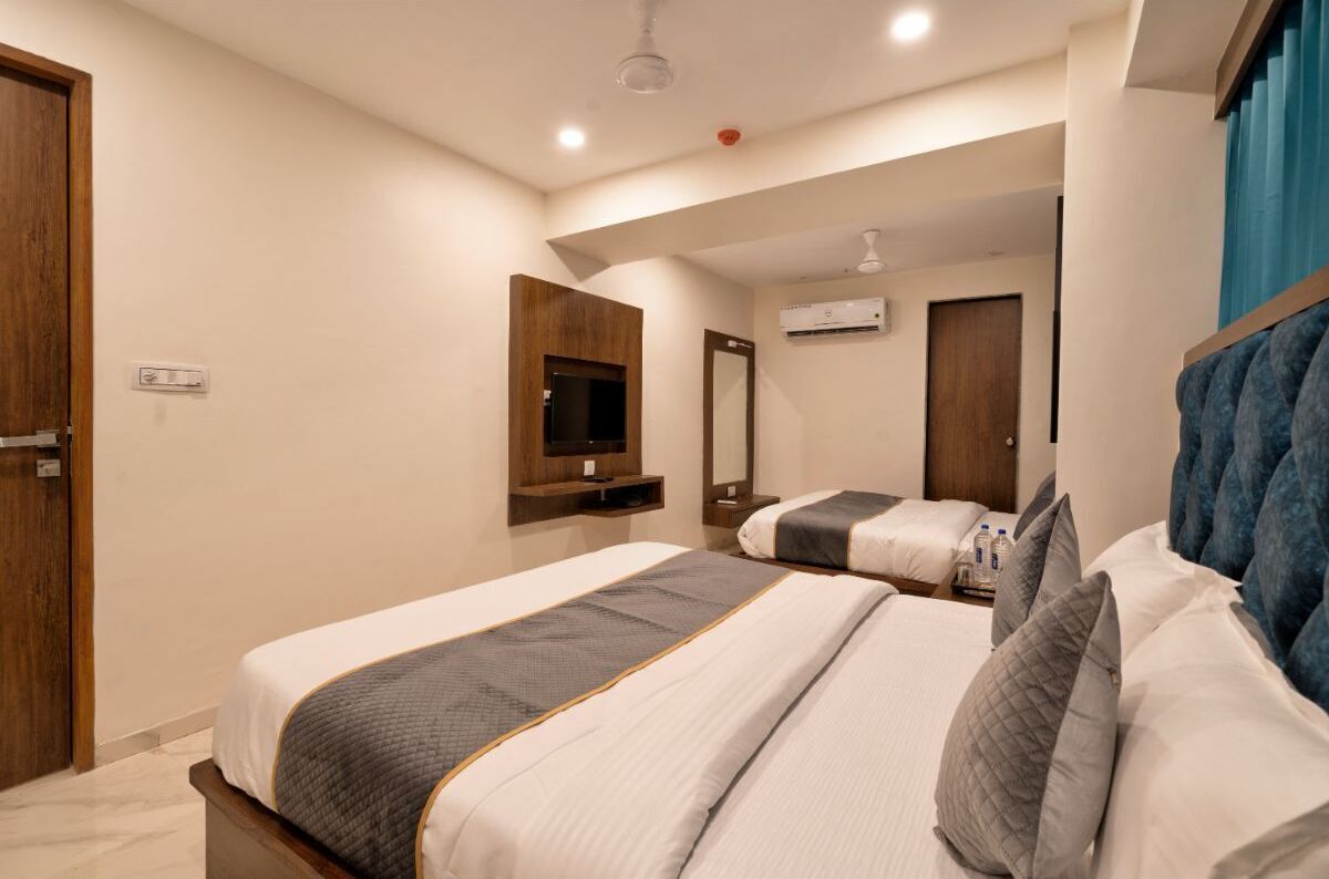 A hotel room with two beds, a TV, a mirror, and an air conditioning unit.