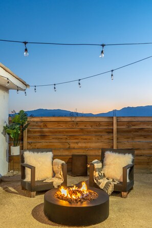An outdoor seating area with a fire pit, two chairs, and a wooden fence.