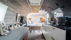 Een ruimtelijk ingerichte camperinrichting met een kitchenette, zithoek en een bed.