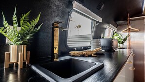 Een moderne keuken met een zwart aanrecht, een roestvrijstalen spoelbak en houten plantenstandaards.