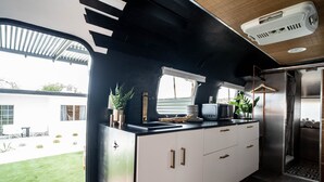 Een moderne keuken met witte kasten, een zwart aanrecht en een ingebouwde magnetron. Er is een raam met zonwering, een hangende plant en een klein spoelbakje.